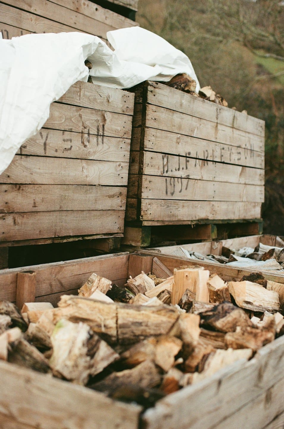 Gestapelte Holzkisten, gefüllt mit gespaltenen Baumstämmen und Brennholz im Freien.